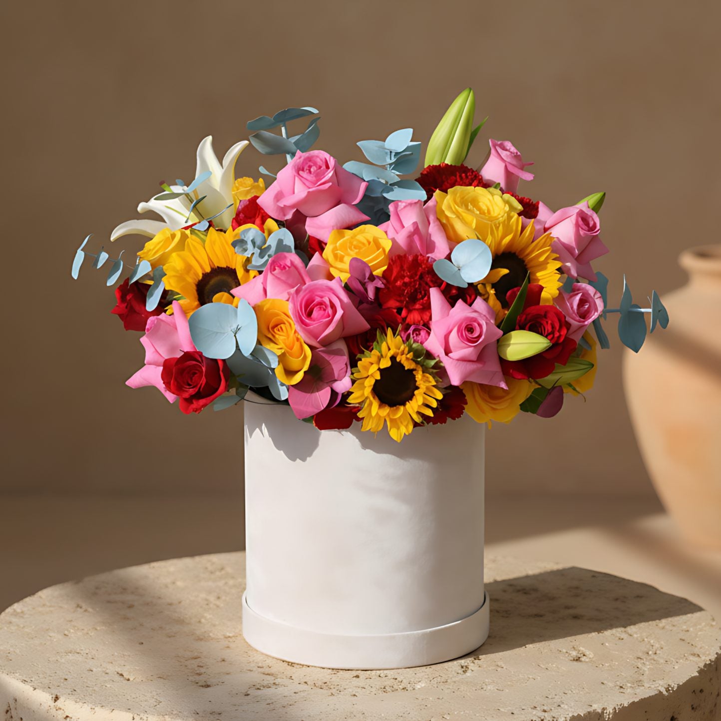 White velvet box arrangement with pink, yellow and red roses, sunflowers, white lilies, and blue eucalyptus