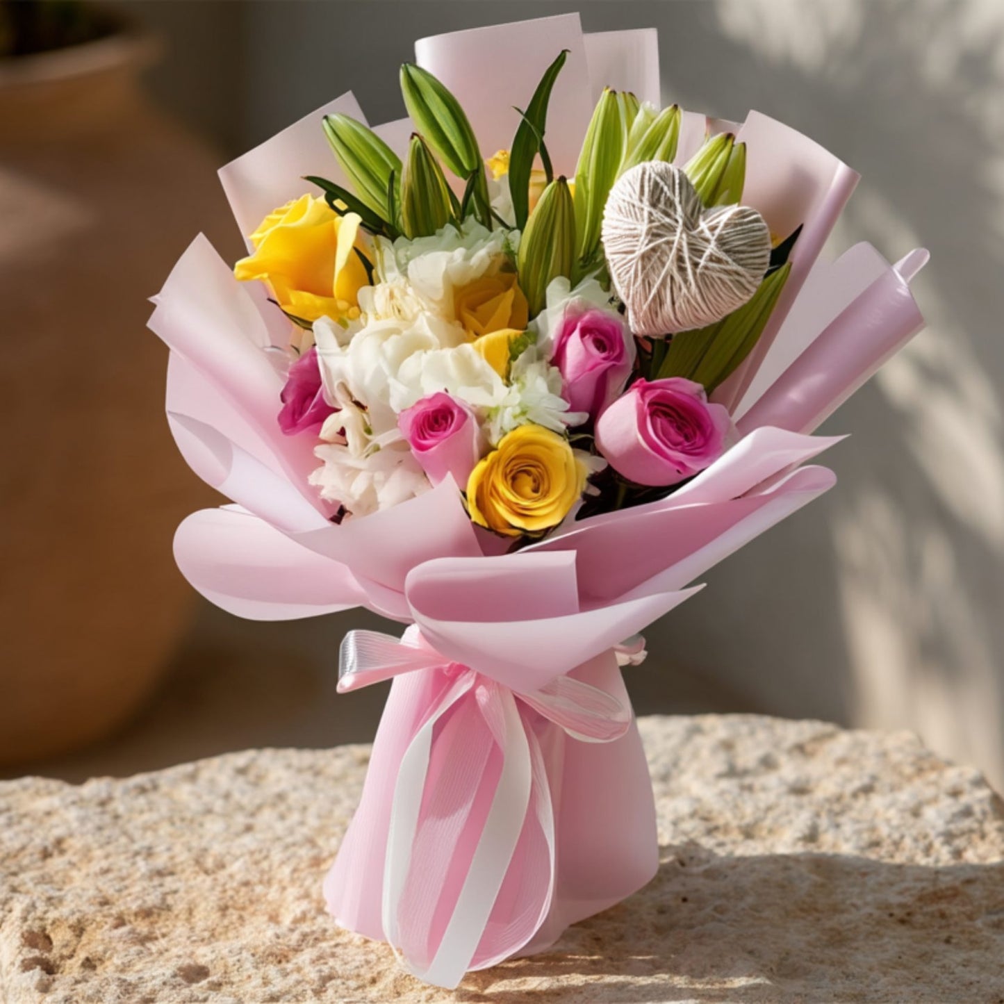 Hand-tied bouquet of pink and yellow roses with white hydrangea, lilies, and a heart detail in soft pink wrapping by Aiwa Flowers Dubai