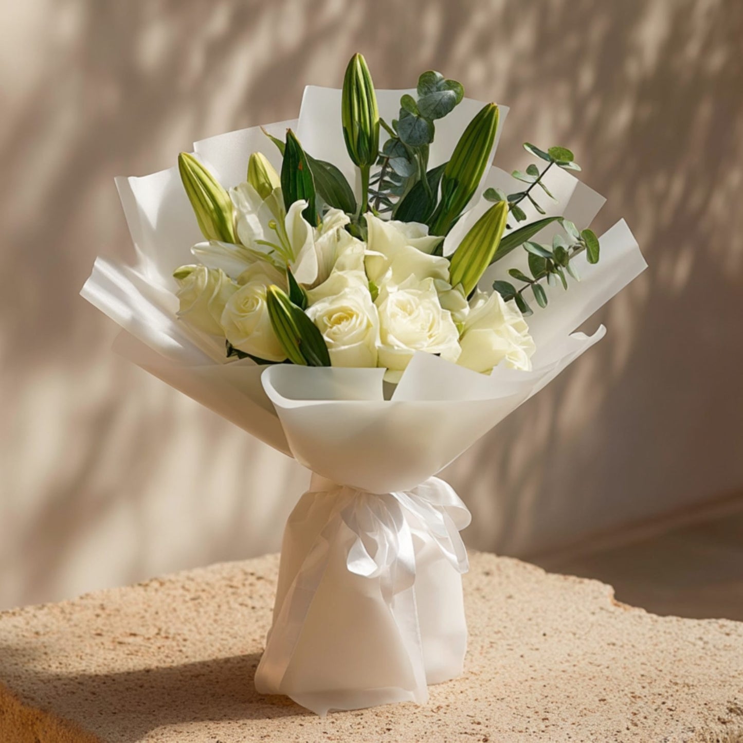 Hand-tied bouquet of white roses with lilies and eucalyptus in elegant white wrapping by Aiwa Flowers Dubai