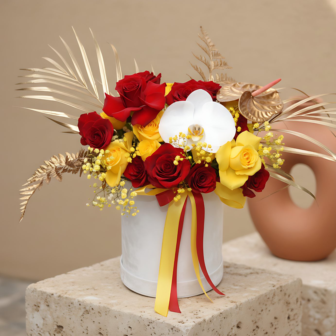 White velvet box arrangement with red and yellow roses, white orchid, yellow gypsophila, and gold accents