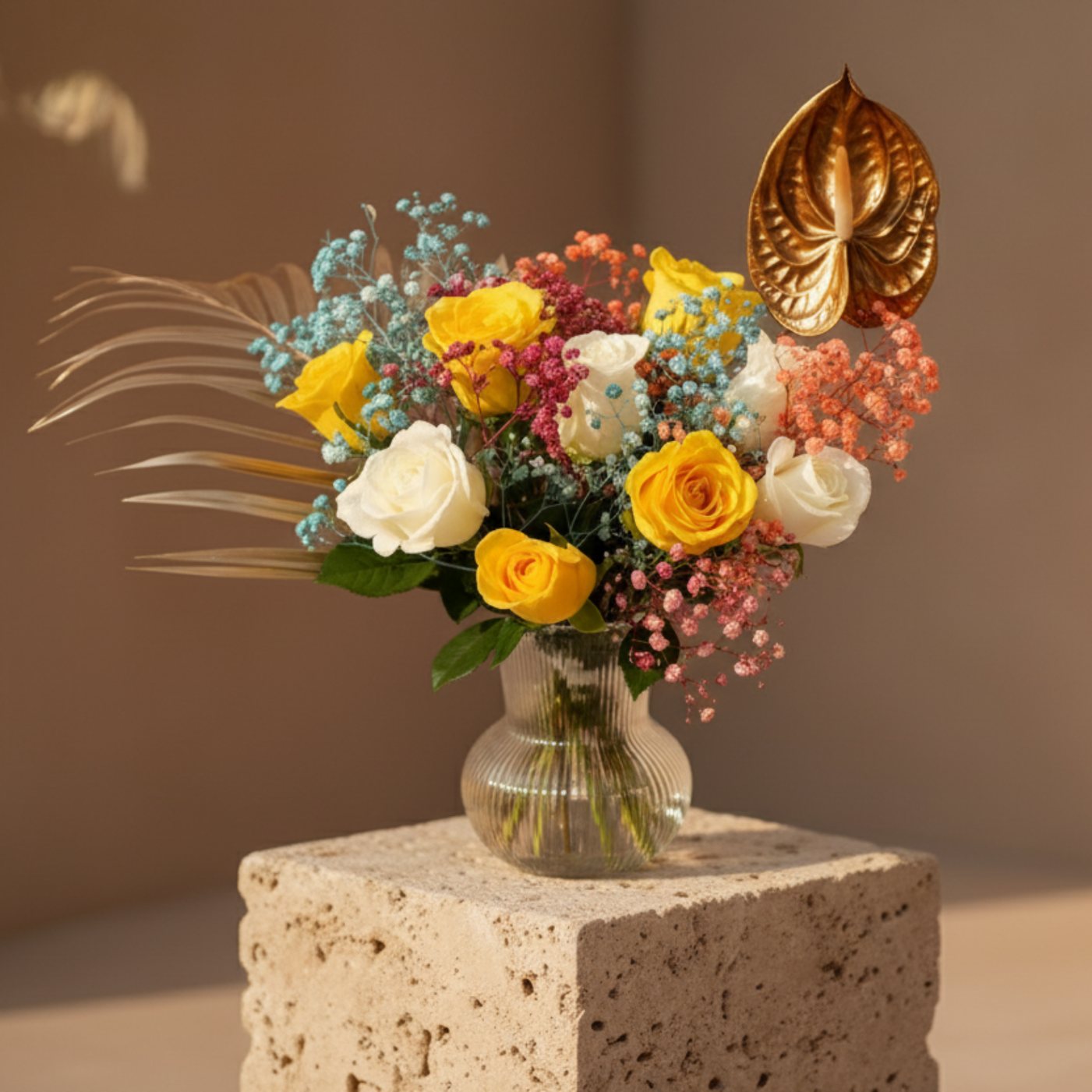Yellow and white rose arrangement with colorful gypsophila and anthurium in a clear glass vase.