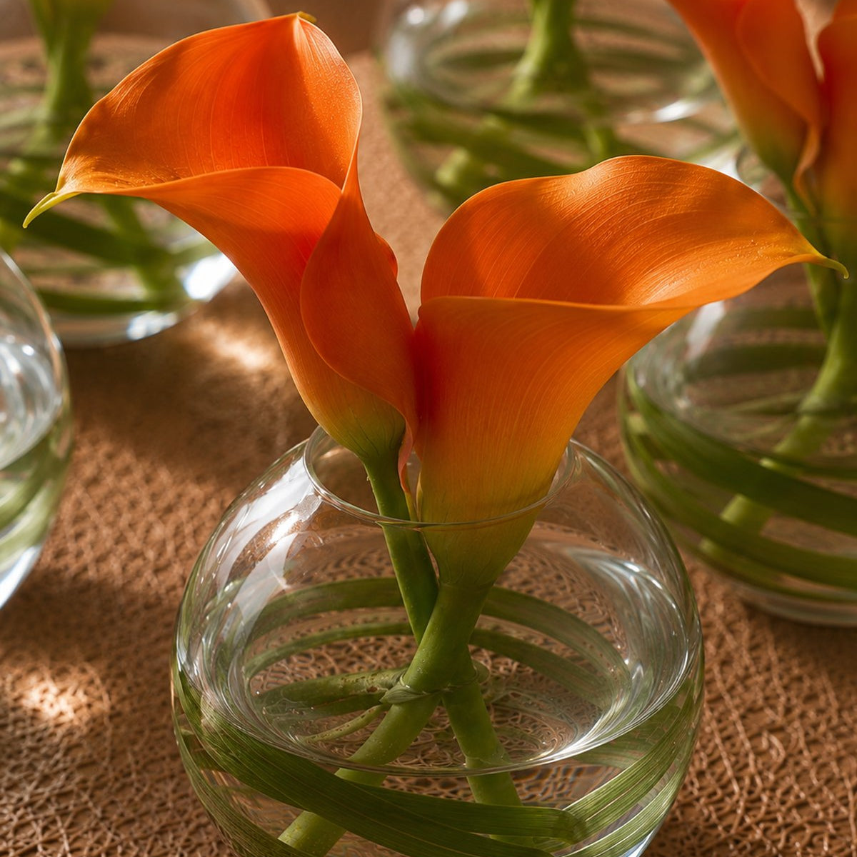 Close-up of orange calla lilies with bear grass in a small clear glass bud vase - Stella by AIWA Flowers