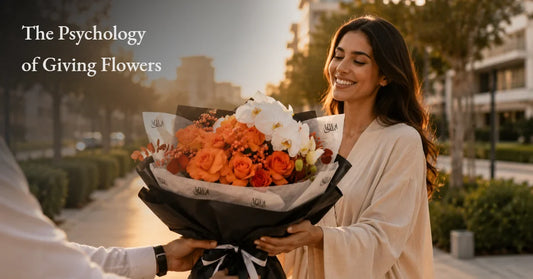 Man surprising a woman with a bouquet of orange roses and white flowers on a sunlit Dubai street, illustrating the psychology of giving flowers