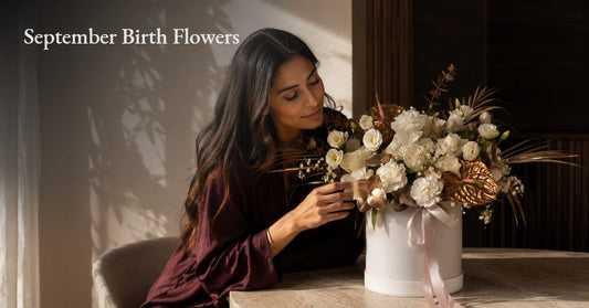 Woman arranging a white and gold September birthday flower bouquet in a round box, AIWA Flowers Dubai