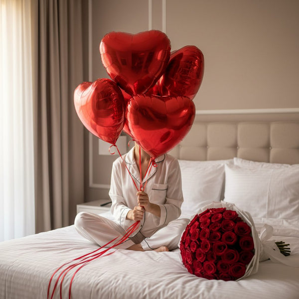 woman sitting on bed holding five red heart balloons with 55 red roses bouquet luxury romantic setup Dubai
