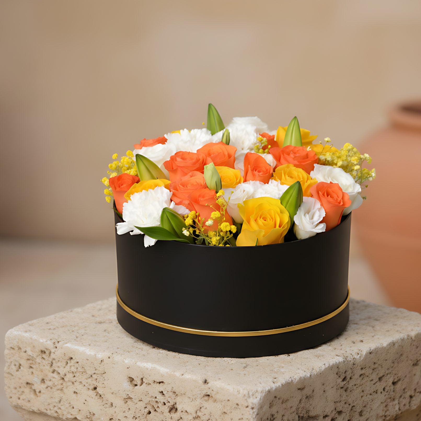 Black box floral arrangement with white, yellow and orange roses, white carnations, lilies, and yellow gypsophila