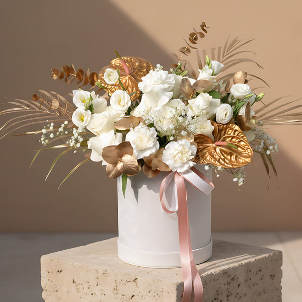 White velvet box arrangement with white roses, carnations, lisianthus, gypsophila, and gold accents