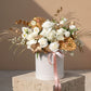 White velvet box arrangement with white roses, carnations, lisianthus, gypsophila, and gold accents