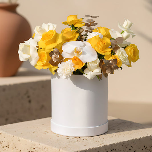 White velvet box arrangement with white and yellow roses, white carnations, orchid, and gold eucalyptus