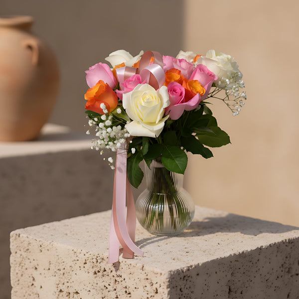 Clear glass vase arrangement with white, pink and orange roses, gypsophila, and decorative ribbon