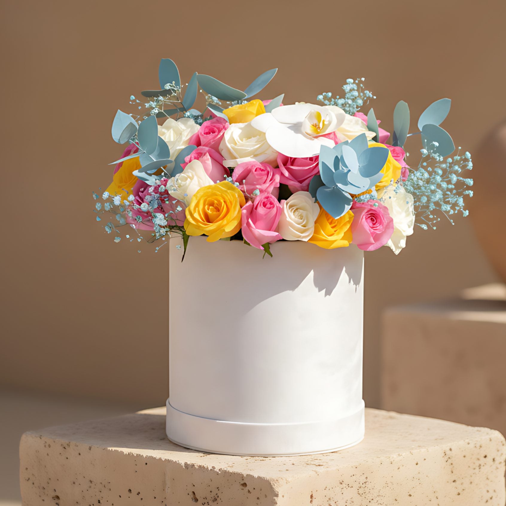 White velvet box arrangement with white, yellow and pink roses, white orchid, blue eucalyptus, and blue gypsophila