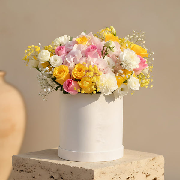 White velvet box arrangement with pink and yellow roses, white carnations, lisianthus, and gypsophila
