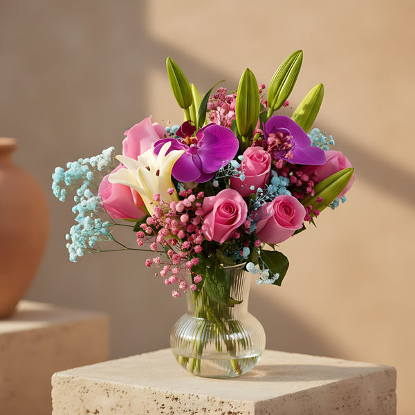 Clear glass vase arrangement with purple orchids, pink roses, lilies, and colorful gypsophila