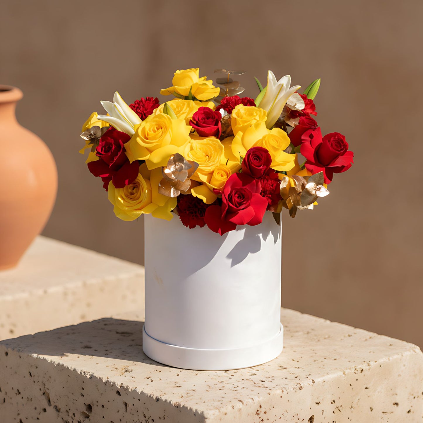 White velvet box arrangement with red and yellow roses, red carnations, white lilies, and gold eucalyptus