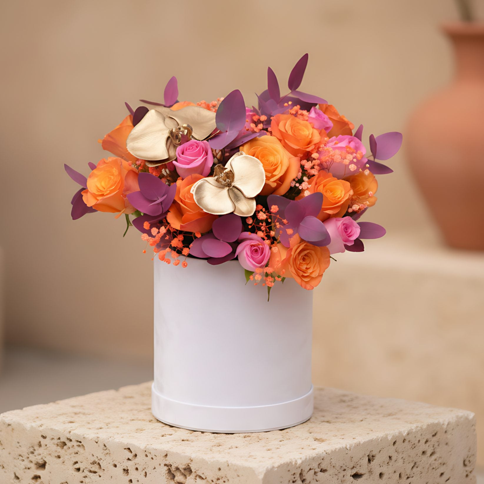 White velvet box arrangement with pink and orange roses, gold orchid stems, eucalyptus, and orange gypsophila