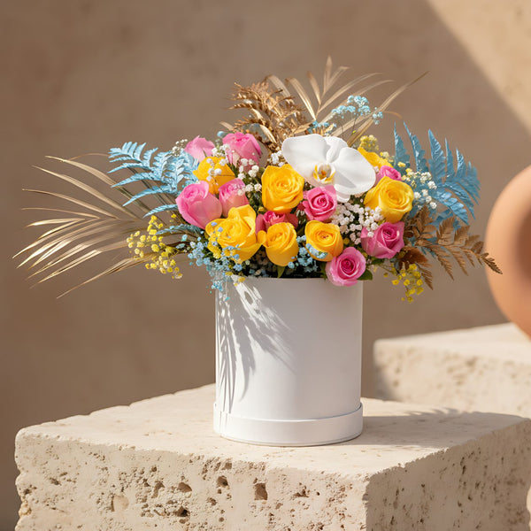 White velvet box arrangement with pink and yellow roses, white orchid, colorful gypsophila, and gold accents