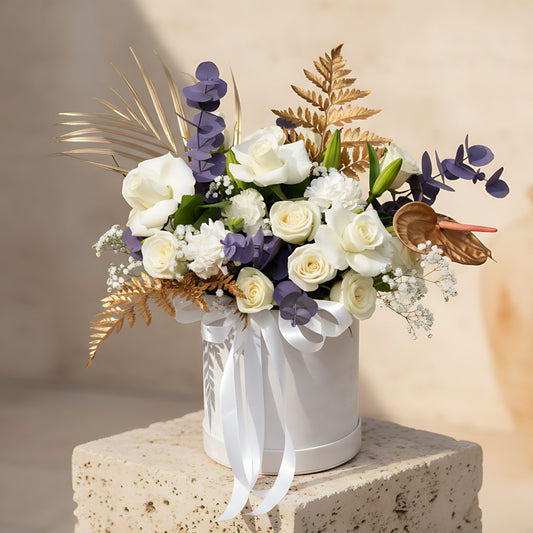 White velvet box arrangement with white roses, carnations, lilies, gypsophila, and gold accents
