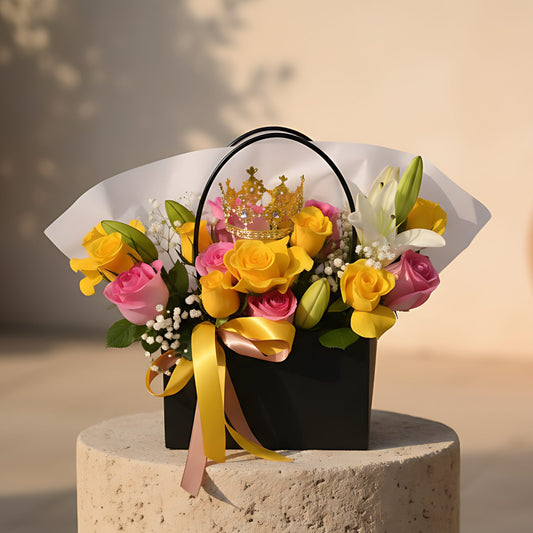 Bag-box floral arrangement with pink and yellow roses, white lilies, gypsophila, and crown accessory