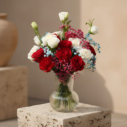 Clear glass vase arrangement with red roses, red and white carnations, lisianthus, and blue and pink gypsophila