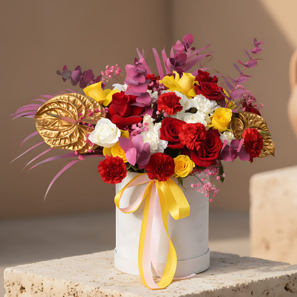 Luxury white velvet box arrangement with mixed roses, carnations, gold anthuriums, and pink accents