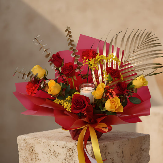 Hand-tied bouquet with yellow and red roses, gypsophila, greenery, and a vanilla candle wrapped in red paper