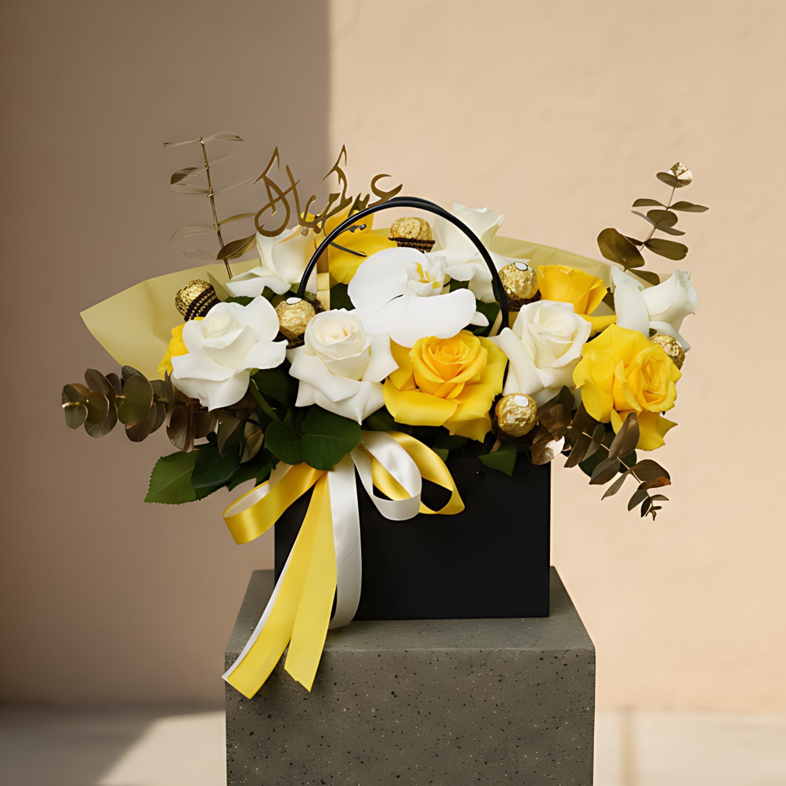 Al Adha Blooms floral arrangement with yellow and white roses, orchid, Ferrero chocolates, and Arabic topper in black bag-box by Aiwa Flowers Dubai
