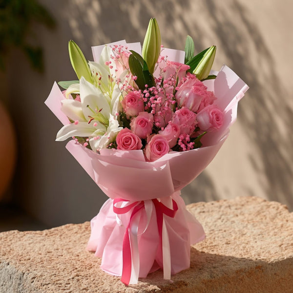 Hand-tied bouquet of pink roses with white lilies and pink gypsophila in soft pink wrapping by Aiwa Flowers Dubai
