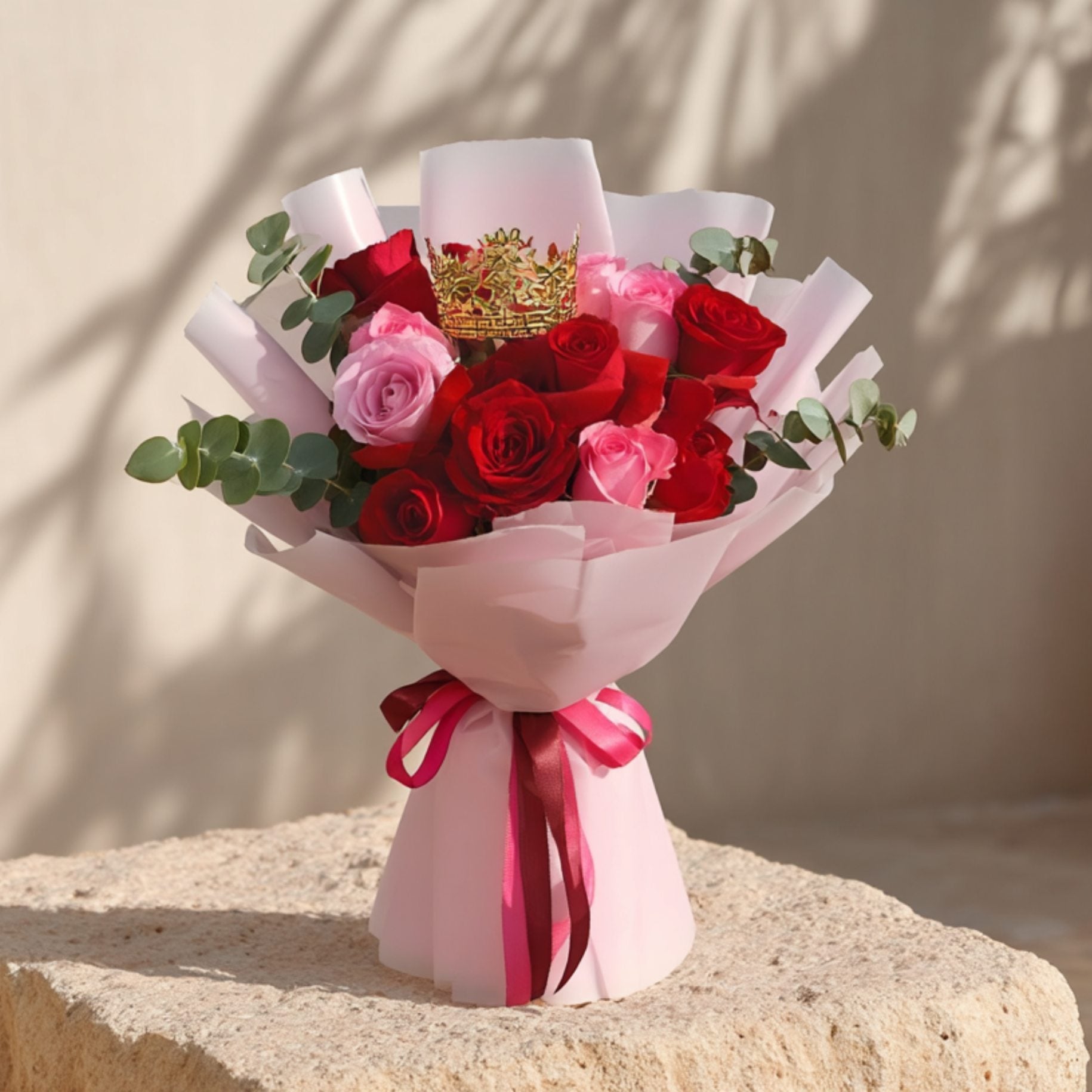 Hand-tied bouquet of red and pink roses with eucalyptus and a crown accessory in soft pink wrapping by Aiwa Flowers Dubai
