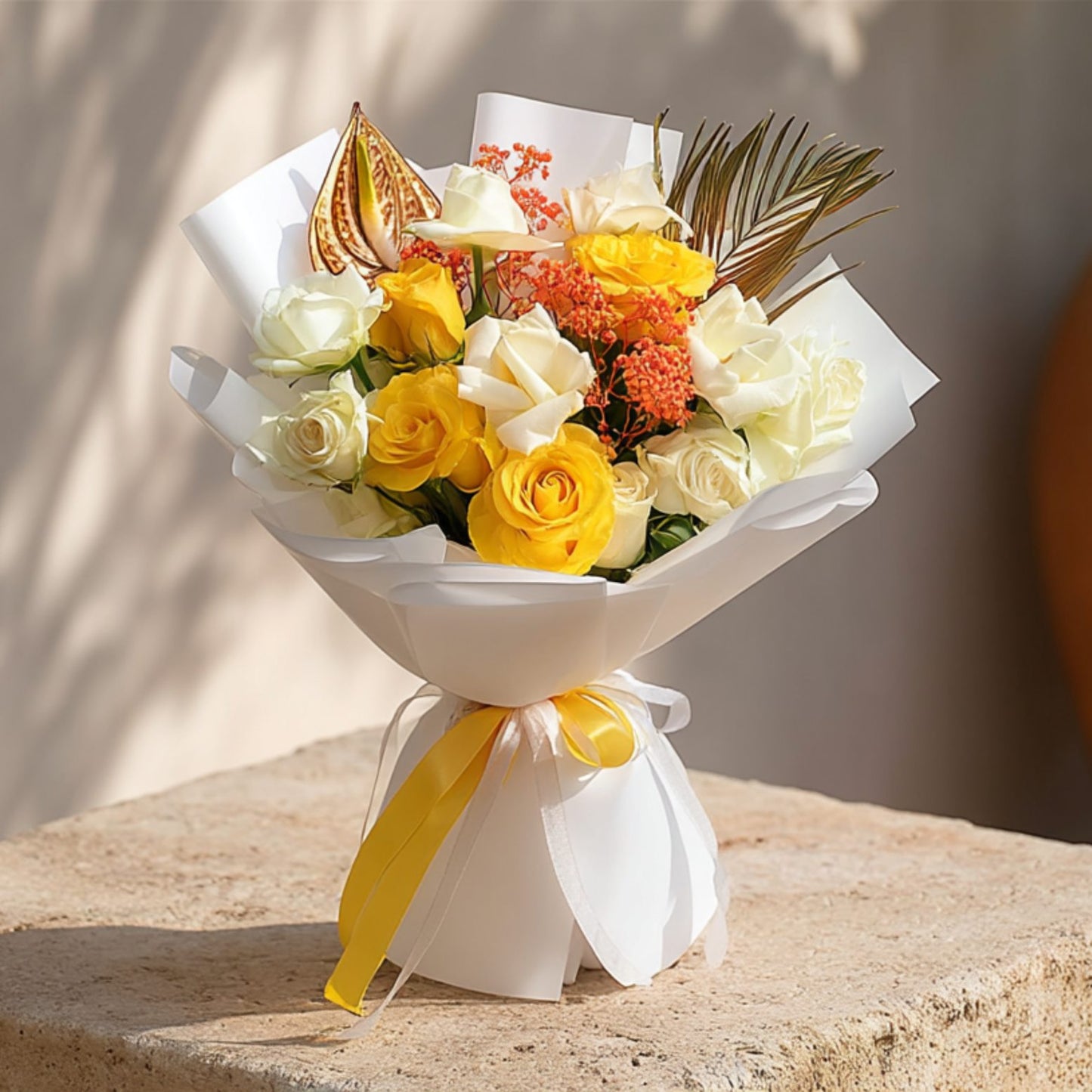Hand-tied bouquet of yellow and white roses with gold anthurium, orange gypsophila, and areca leaf in white wrapping by Aiwa Flowers Dubai
