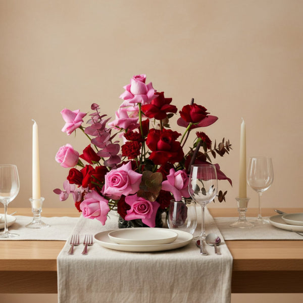 Blush pink and deep red rose floral centerpiece arranged on an elegant dining table setting.