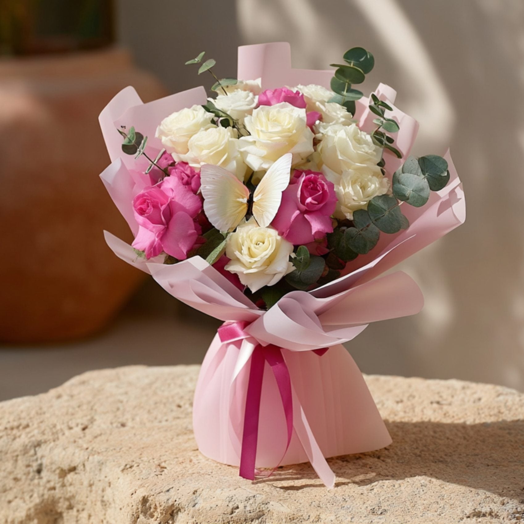 Hand-tied bouquet of white and pink roses with eucalyptus and a butterfly accent in soft pink wrapping by Aiwa Flowers Dubai
