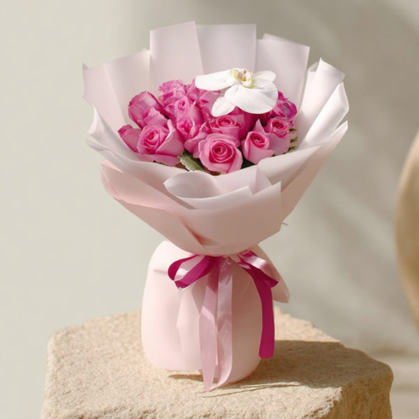 Hand-tied bouquet of 20 pink roses with a white orchid in soft light pink wrapping, handcrafted by Aiwa Flowers in Dubai
