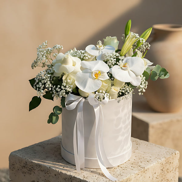 Fiancé white velvet round box arrangement with white orchids, white roses, lily, eucalyptus, and gypsophila by Aiwa Flowers Dubai