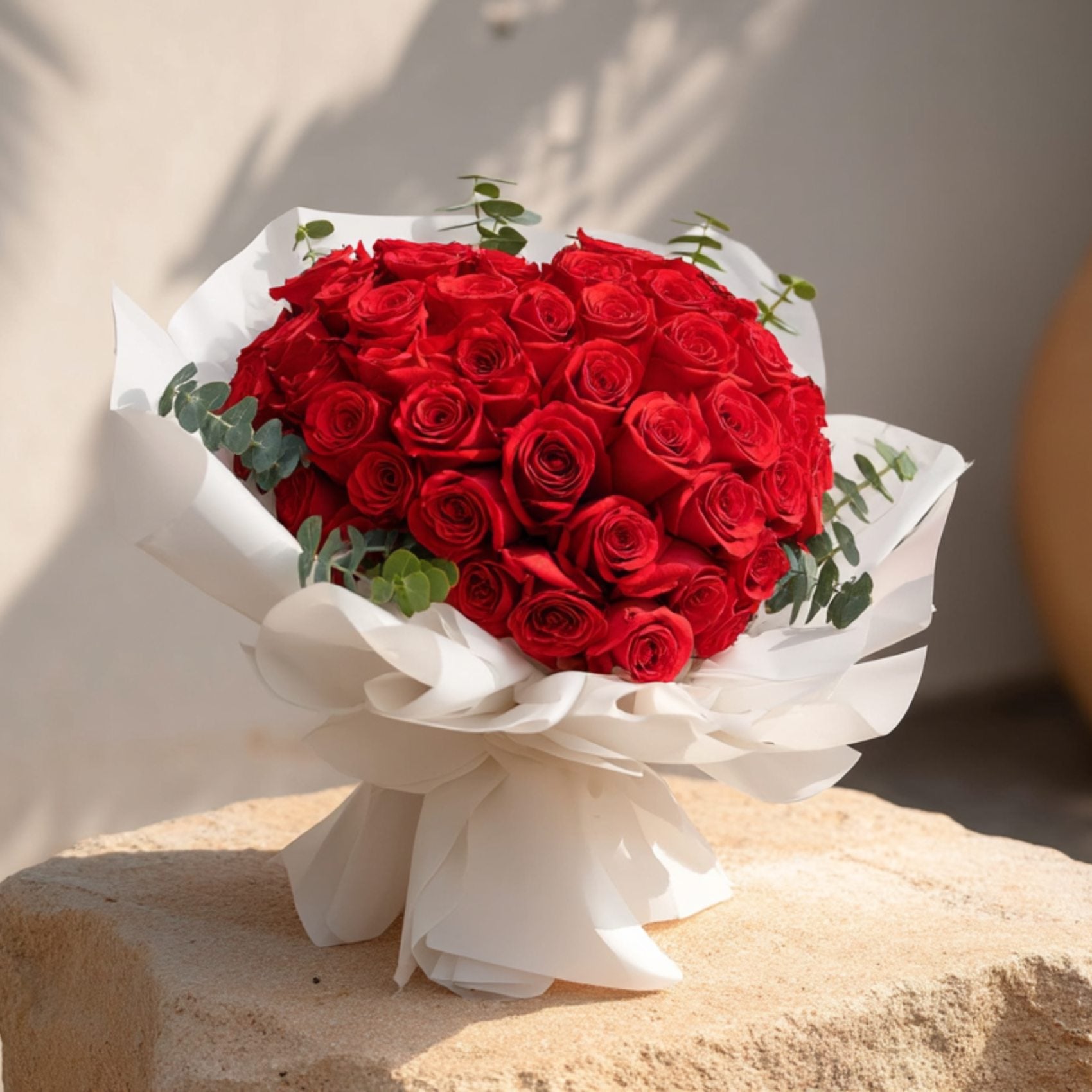 Heart-shaped hand-tied bouquet of red roses in elegant white wrapping by Aiwa Flowers Dubai
