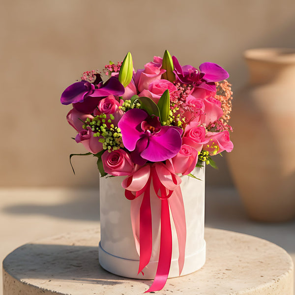 Fucsia white velvet round box arrangement with purple orchids, pink roses, lilies, and gypsophila by Aiwa Flowers Dubai