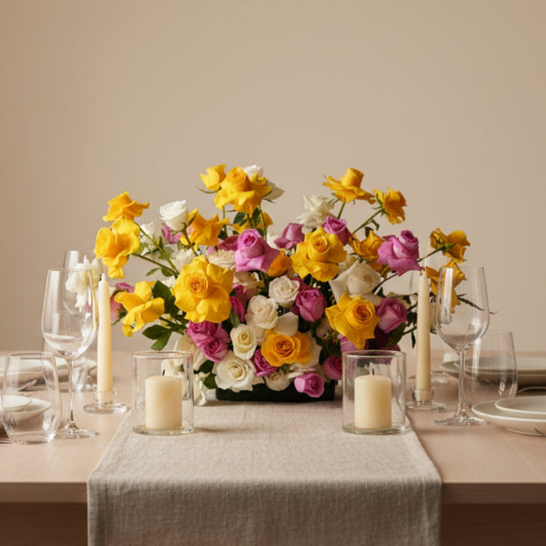 Colorful garden-style centerpiece with yellow, blush, and ivory roses arranged on an elegant dining table.