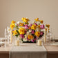Colorful garden-style centerpiece with yellow, blush, and ivory roses arranged on an elegant dining table.