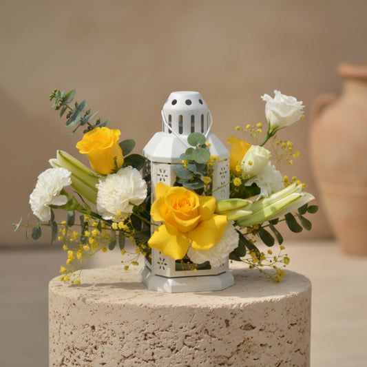 Jawaher floral arrangement with white lilies, yellow and white roses, carnations, lisianthus, and eucalyptus in a white lantern by Aiwa Flowers Dubai