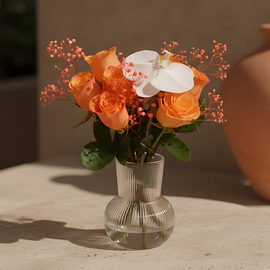 Kylie floral arrangement with orange roses, white orchid, and orange gypsophila in a clear glass vase by Aiwa Flowers Dubai