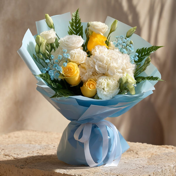 Hand-tied bouquet of white and yellow roses with hydrangea, lisianthus and blue gypsophila in blue wrapping by Aiwa Flowers Dubai
