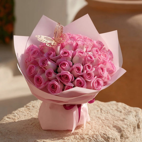 Hand-tied bouquet of 55 pink roses with butterfly accent in soft pink wrapping by Aiwa Flowers Dubai
