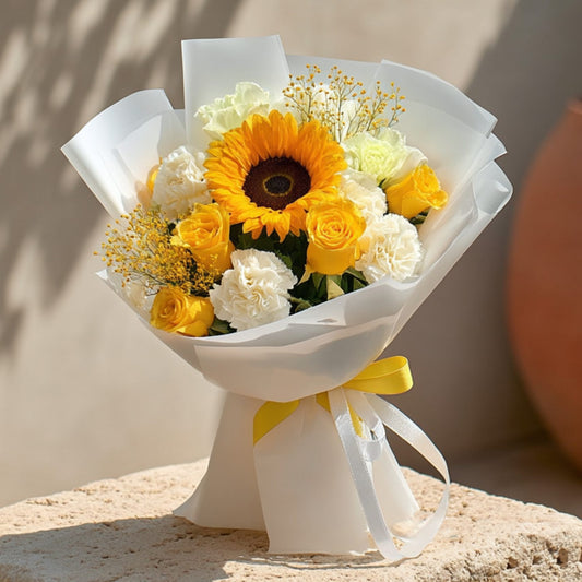 Hand-tied bouquet with a sunflower, yellow and white roses, carnations, and yellow gypsophila in white wrapping by Aiwa Flowers Dubai