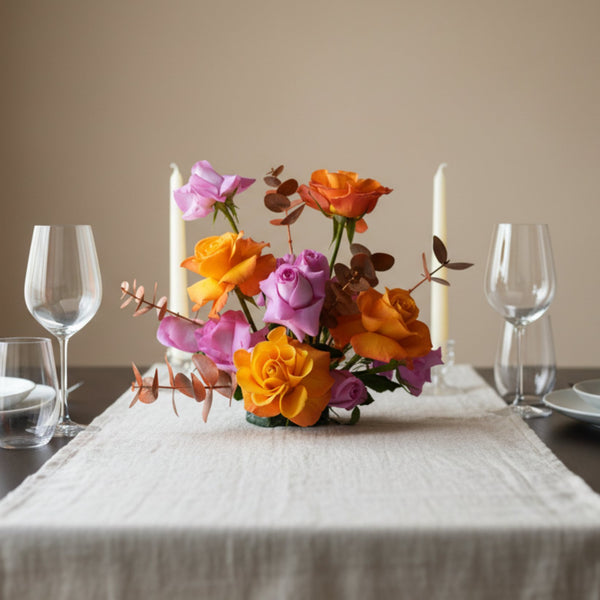 Sunset-toned centerpiece with orange and blush roses arranged on an elegant dining table setting.
