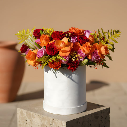 Vermillion velvet box arrangement with orange, pink, and red roses, red carnations, white lilies, and fern leaves by Aiwa Flowers Dubai