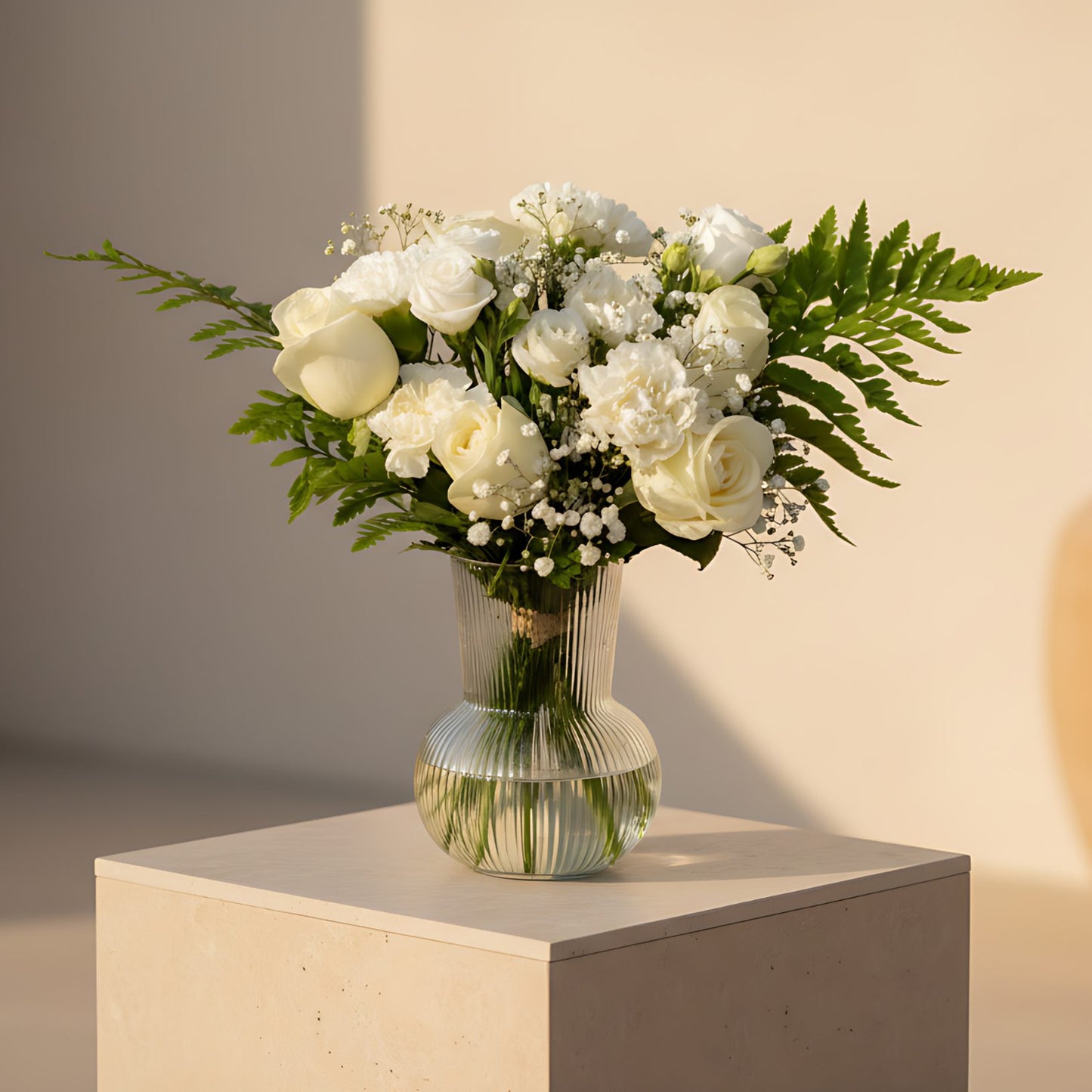 Clear glass vase arrangement with white roses, white carnations, lisianthus, fern leaves, and gypsophila