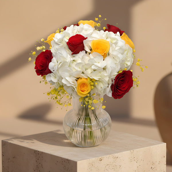 Clear glass vase arrangement with red and yellow roses, white hydrangea, and yellow gypsophila