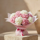 Bouquet of pink and white hydrangeas wrapped in soft pink paper with ribbon on a stone pedestal.