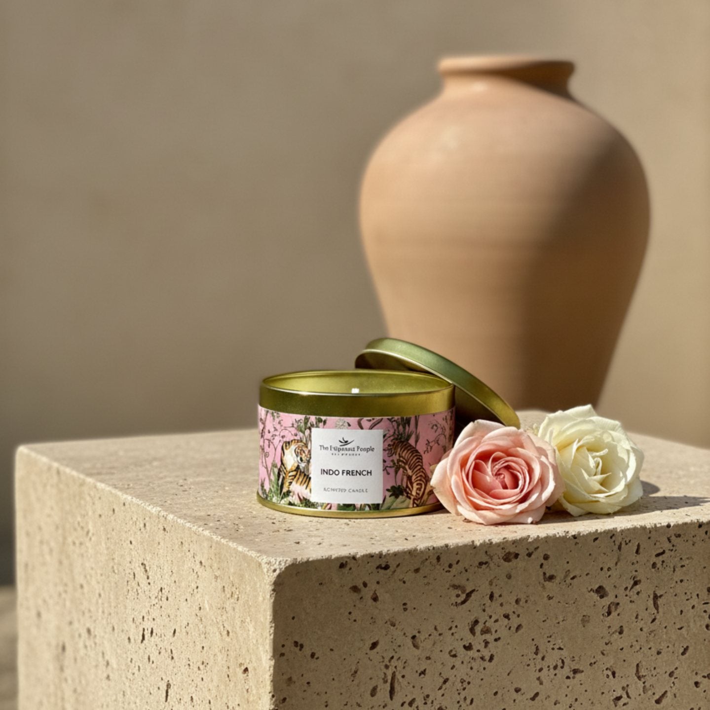Indo French scented candle in decorative tin with gold lid placed on beige pedestal with roses