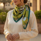Model wearing green floral silk scarf styled around neck in elegant fashion look.