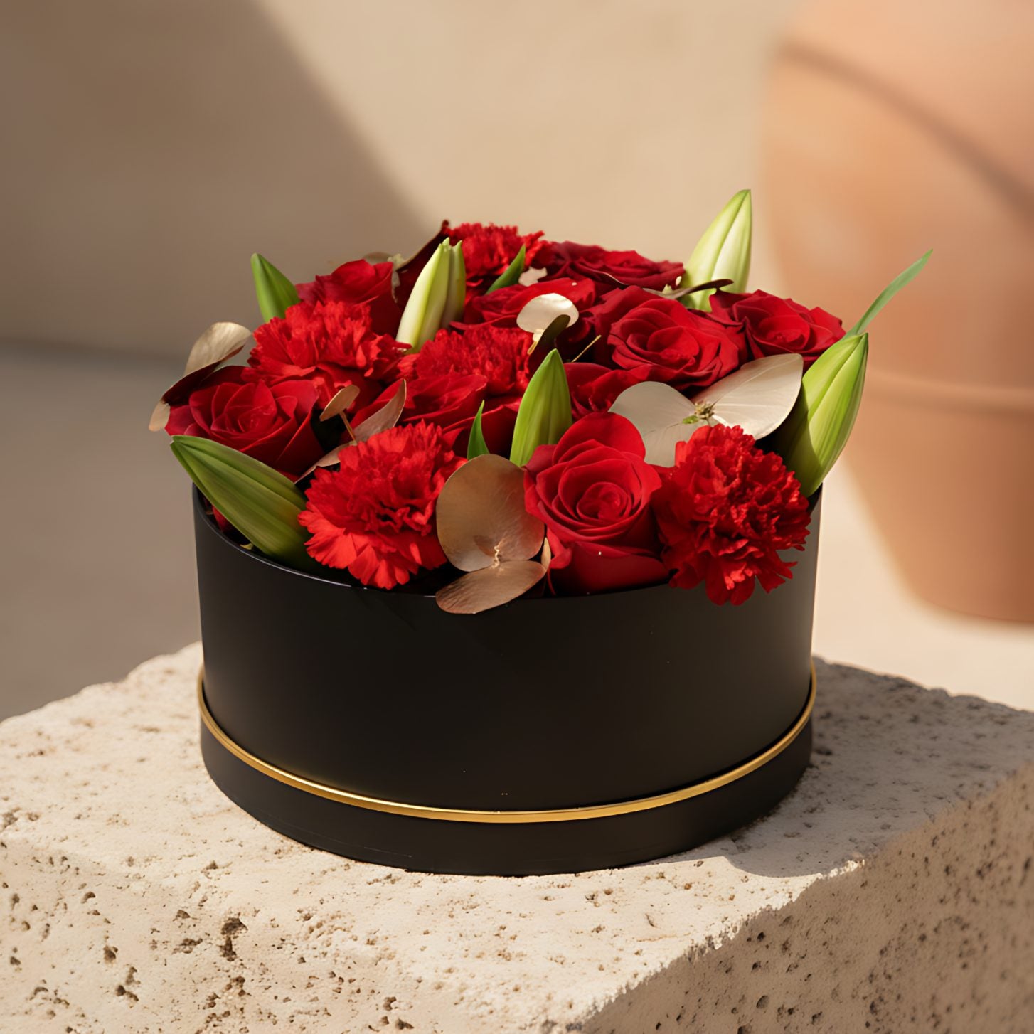 Black box flower arrangement with red roses, red carnations, white lilies, and gold eucalyptus